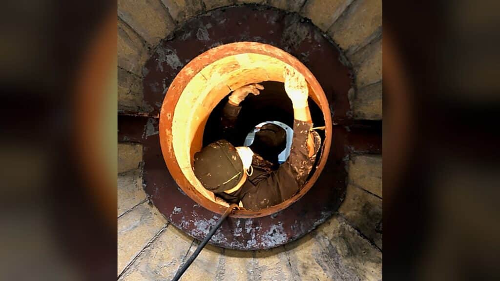 Technician performing commercial boiler cleaning through a boiler access opening