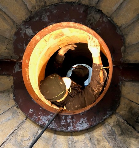 Technician performing commercial boiler cleaning through a boiler access opening