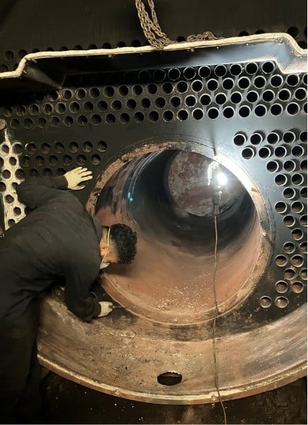Technician inspecting the furnace tube of a commercial fire-tube boiler during cleaning and inspection